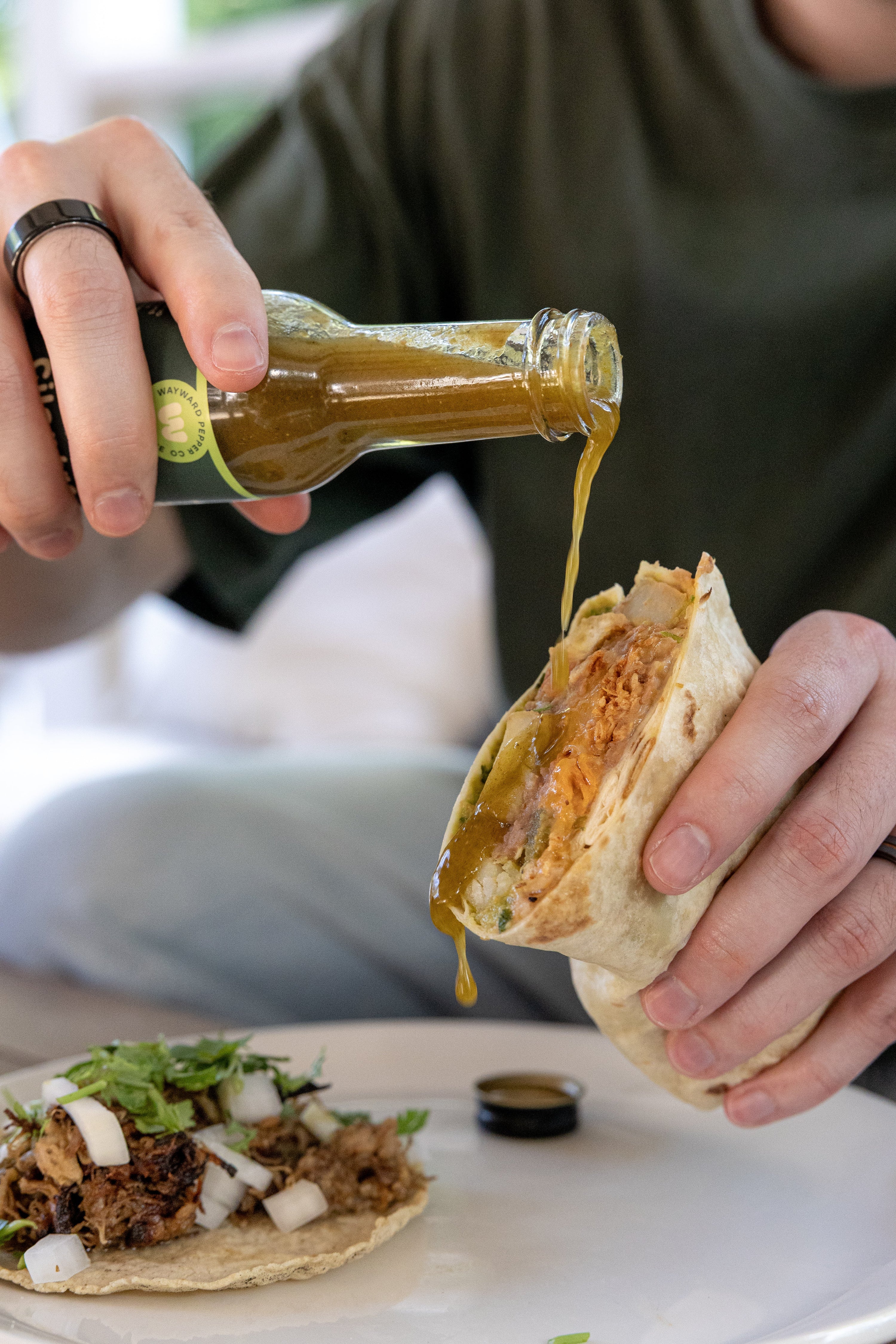 Green Jalapeño Cilantro hot sauce being poured onto a burrito